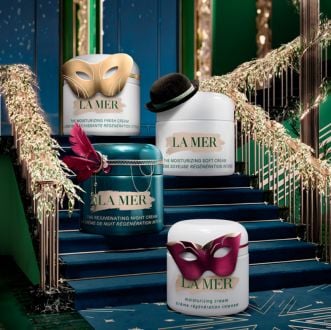 Close up of model applying Crème de la Mer to cheek, in bright, ambient lighting