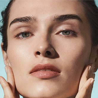 Close up of model applying Crème de la Mer to cheek, in bright, ambient lighting